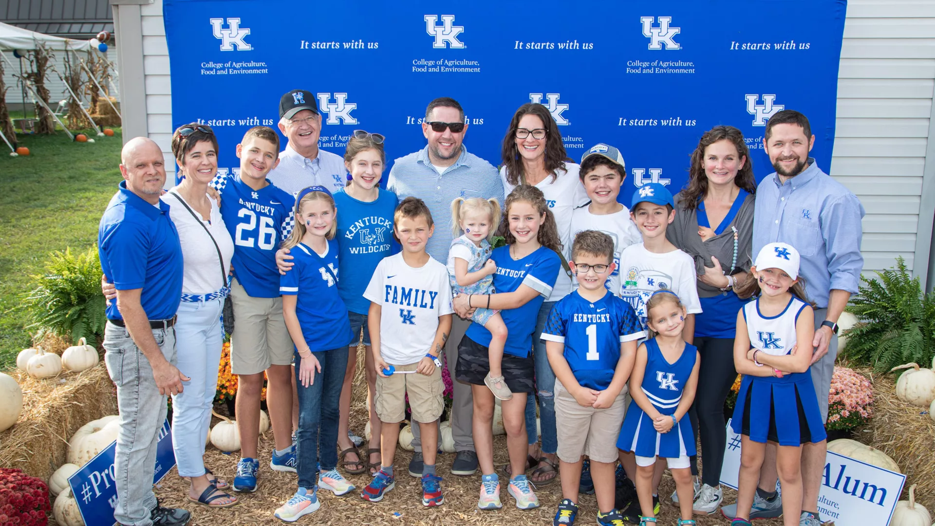A big family poses in front of a UK M-G CAFE backdrop